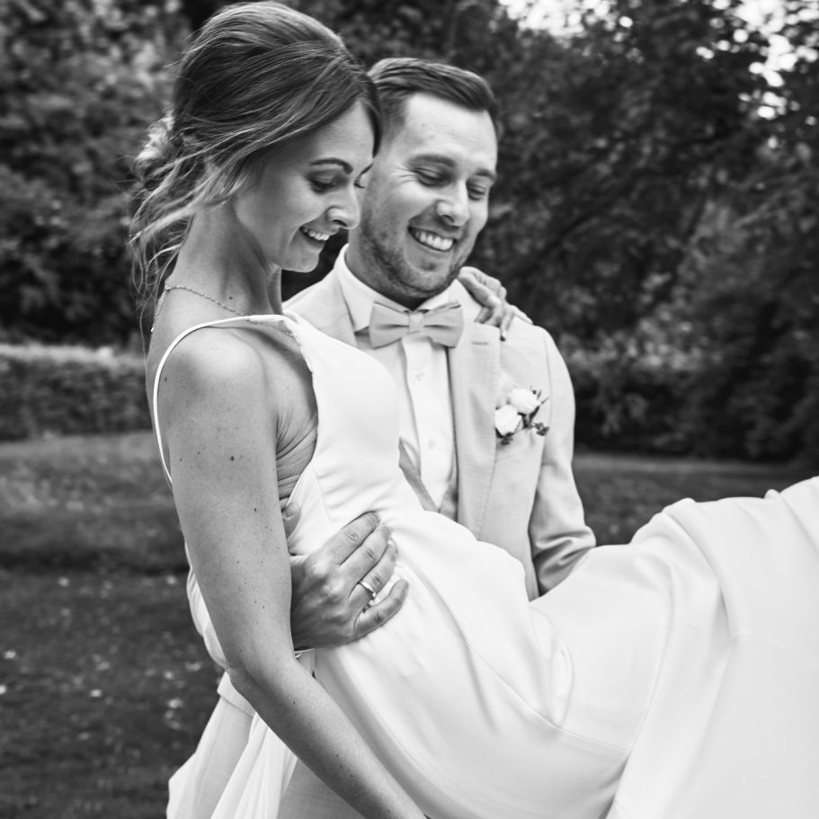 Hochzeitsfotografie auf dem Uphof in Bielefeld Der Bräutigam hält die Braut beim Paarshooting auf dem Uphof in Bielefeld während der Sommerhochzeit im Grünen